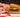 a thick Halal burger patty with a sesame bun, pickles, tomatoes, and cheese on top and lettuce under it sits on a plate with fries around it.