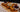 A serving board with an assortment of golden-brown fried thanksgiving leftover balls stuffed with turkey, stuffing, and mashed potatoes next to dishes of cranberry sauce and brown gravy.