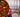 Top down image of a large red pot of beef stew made with chunks of red potato, sliced carrots, peas, green beans, and tender chunks of beef served next to a wood serving tray with an empty bowl and small loaf of bread, all served on a striped tablecloth.