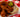 Top-down image of spicy fried chicken piled up on top of white bread and topped with pickle slices, served on a white plate on a red and white checkered tablecloth.
