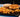A double cheeseburger with two beef patties and cheese between slices of fried onion, served with fries and a white bowl of sauce. All served on a black plate on a white and blue striped tablecloth.