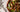 Top down image of a salad of greens, black olives, sliced green pepperoncini, white mozzarella, red pepperoni pieces, and brown breadcrumbs with a red tomato dressing in a brown wood bowl on a white and black marble table.