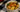 A tan ramekin of hearty tortellini soup, filled with tender celery, carrots, tortellini, and spinach with bits of juicy Halal chicken.