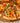a close up of a taco pizza that sits on a round wooden serving tray. The taco pizza is topped with chips, lettuce, tomatoes, and midamar halal taco beef.