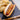 A halal beef frank in a hot dog bun with mustard on it sits on a black cutting board with potato chips behind it.