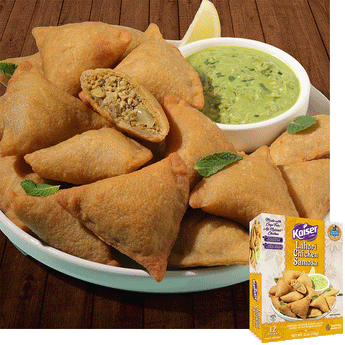 Kaiser Lahori Chicken Samosas in a pile on a white plate with some mint leaves. A bowl of chutney sits next to the pile. One samosa is cut in half and a minced meat mixture is visible inside. A package of Kaiser Lahori Chicken Samosa is overlaid in the bottom right corner.