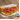 a chicken bologna sandwich on white bread. The chicken bologna is piled high on a bed of American cheese, alfalfa sprouts, lettuce, and a white condiment. At the back of the plate is a small pile of chips. A package of Midamar Chicken Bologna is overlaid in the bottom right corner.