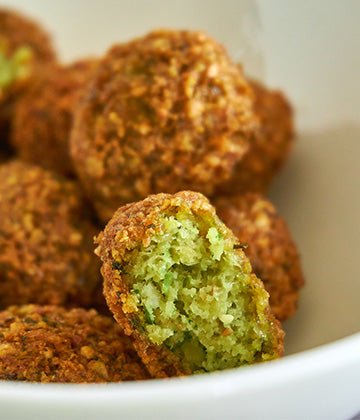 a close up of a bowl of falafel, the front most falafel is ripped in half to expose the insides
