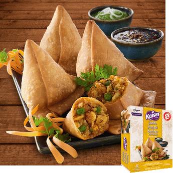 Jumbo punjabi samosas sit on a black plate. One samosa is cut in half to reveal the filling. The plate is garnished with strips of carrot and pieces of cilantro, in the background is a green sauce with onion strips and black chili sauce. In the bottom right hand corner is an image of the product package