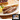 3 Midamar beef brakfast links on a white plate. A pile of scrambled eggs with a piece of basil on top of it are to the left and a piece of white toast with grape jelly on it and a plain piece of toast are behind them. A package of Midamar Breakfas links is overlayed on top of the package.