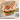 A turkey sandwich with oats baked into the top of the bread. The sandwich is piled high with Midamar halal turkey which is resting on a slice of cheese, tomatoes, and lettuce. In the bottom corner is an image of the product package