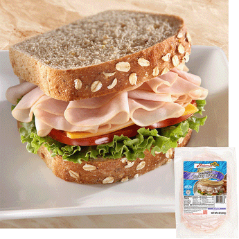 A turkey sandwich with oats baked into the top of the bread. The sandwich is piled high with Midamar halal turkey which is resting on a slice of cheese, tomatoes, and lettuce. In the bottom corner is an image of the product package