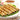 Malai kababs resting on a bed of lettuce on a white plate. In the background is garnishing and a brown sauce
