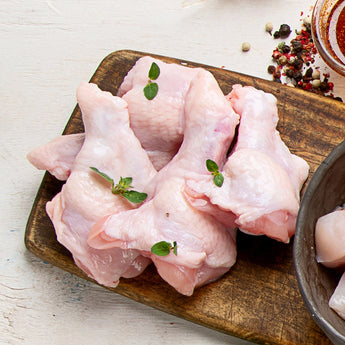 raw chicken drumettes sit on a dark wooden board. The drumettes are garnished with green herbs