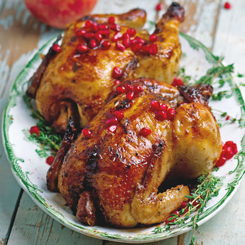 two cooked cornish hens on a white and green platter. The hens are garnished with pomegranate arils