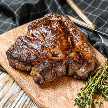 A halal chuck roast with char on a wood cutting board with a sprig of thyme