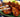 A Halal chicken drumstick leans on a larger chicken thigh both are glazed with bbq sauce. 