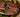 Medium-rare grilled steak cut into slices, served on top of a salad of greens and avocado in a wooden bowl, on a tan tablelcoth.