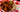 Top-down image of spicy fried chicken piled up on top of white bread and topped with pickle slices, served on a white plate on a red and white checkered tablecloth.