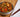 A small white bowl of fried noodles with chunks of chicken, carrots, and green onion next to a white napkin and wood chopsticks on a bamboo placemat.