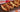 An assortment of chicken sandwiches with chunks of chicken, sliced red peppers and onion, and melted cheese on hotdog buns. All served on a black serving board on a vibrant background.