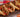An assortment of chicken sandwiches with chunks of chicken, sliced red peppers and onion, and melted cheese on hotdog buns. All served on a black serving board on a vibrant background.