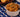 A small bowl of hamburger helper, with Cellentani pasta noodles and Halal ground beef coated in a cheesy tomato sauce and topped with parsley. Served in front of a wooden bowl of garlic bread in the background.