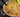 A tan ramekin of white chicken chili with chunks of juicy Halal chicken breast, organic corn, cannellini beans. Topped with shredded cheese and served with slices of avocado.