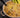 A tan ramekin of white chicken chili with chunks of juicy Halal chicken breast, organic corn, cannellini beans. Topped with shredded cheese and served with slices of avocado.