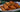A stack of golden-brown fried Halal chicken egg rolls stuffed with shredded carrots, cabbage, aromatics, and pieces of juicy Halal chicken breast served on a white and blue ornate plate.