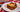 A slice of lasagna, with layers of Halal meat sauce, cheese filling, and tender lasagna noodles all topped with golden brown melted cheese. Served on a white plate on a red and white checkered tablecloth.