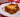 A slice of lasagna, with layers of Halal meat sauce, cheese filling, and tender lasagna noodles all topped with golden brown melted cheese. Served on a white plate on a red and white checkered tablecloth.