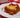 A slice of lasagna, with layers of Halal meat sauce, cheese filling, and tender lasagna noodles all topped with golden brown melted cheese. Served on a white plate on a red and white checkered tablecloth.