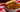 A white bowl with rotini pasta in a meaty red sauce with chunks of Halal ground beef, bacon, and pepperoni. Served with a breadstick on a red and white checkered tablecloth.