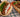 Golden-brown lamb meatballs, served on a pita with tomatoes, lettuce, and tzatziki sauce alongside a wooden platter with rice, veggies, and topped with more meatballs.