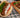 Golden-brown lamb meatballs, served on a pita with tomatoes, lettuce, and tzatziki sauce alongside a wooden platter with rice, veggies, and topped with more meatballs.