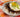 A plate of white rice topped with a savory sauce, juicy Halal burger patties, and a sunny side up egg and sprinkled with savory green onion.
