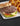 A burger rests on a bun with lettuce, tomato, and american cheese. Beside it are fried onion rings