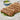 chicken seekh kababs resting leaves of lettuce. The food sits on a rectangular white plate. In the background sits a blow bowl with a beige sauce