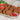 Chicken shami kababs sitting on a rectangular plate. On the back of the plate rest slices of tomato and a leaf of lettuce, on the front of the plate is small bowl with a red condiment.