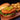 A gourmet chicken sandwich on a wooden board, featuring a golden-brown bread bun, a crispy fried chicken patty topped with pickle slices, fresh lettuce, and tomato, served with a side of tater tots.