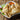12 crispy samosas are piled together on a white plate. A samosa in front is cut open and inside is some ground beef with pieces of vegetables. A bowl of orange sauce sits behind the samosas