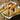 A white plate with crispy chicken samosas resting on a bed of lettuce. The samosas are garnished with a slice of radish and served with a bowl of reddish orange sauce