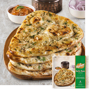 A stack of 4 garlic naan sit in a shallow wooden bowl. In the background is a white cup with red onions, a white cup with a red sauce, and a brass colored vase. In the bottom right hand corner is an image of the product package