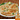 2 Keema paratha are on a plate half of one is stiting one top. Inside the paratha is a ground lamb and hcicken mix with small pieces of vegetables. There are a few pieces of cilantro spread around them.  A box of Kaiser Keema Paratha is in the bottom right corner. 